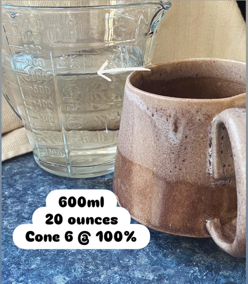 May include: A clear glass measuring pitcher with metric and imperial markings filled with liquid, positioned next to a brown ceramic mug. Text on the image reads 600ml, 20 ounces, and Cone 6 @ 100%. A white arrow points from the pitcher to the mug.