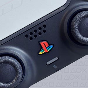 Könnte beinhalten: Weiß-schwarzer PlayStation 5 Anniversary Edition Controller. Der Controller hat eine weiße Oberseite mit schwarzen Akzenten, einschließlich der Analogsticks und Tasten. Das PlayStation-Logo ist sichtbar, zusammen mit dem Text "Anniversary Edition."