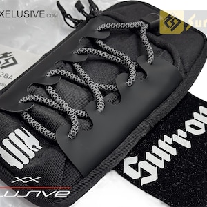 May include: Black carry case with a unique design featuring a black rubber overlay and gray and white rope-style laces. Includes a black wristband with white text. The case has a zipper closure.