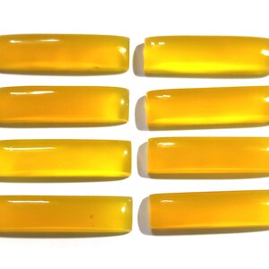 Pode incluir: Oito pedras preciosas retangulares polidas em um tom amarelo vibrante são dispostas em uma superfície branca. As pedras têm bordas arredondadas e um acabamento brilhante, refletindo a luz. Ideal para a fabricação de joias.