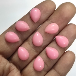 May include: Nine polished, teardrop-shaped gemstones in a soft pink hue. The stones are smooth and evenly coloured, with a slight sheen. They are displayed on a neutral background.