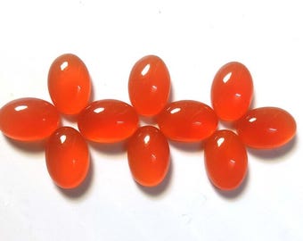 May include: A collection of ten oval-shaped, polished gemstones in a vibrant orange hue. The gemstones are arranged on a white surface, showcasing their smooth, glossy texture and translucent quality. The stones vary slightly in size.