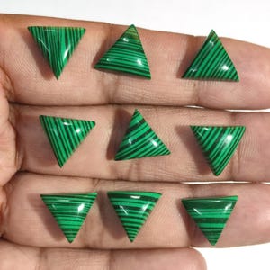 Puede incluir: Nueve piedras preciosas triangulares de malaquita con un vibrante patrón de rayas verdes y negras. Las piedras preciosas están pulidas y tienen una superficie lisa y brillante. Los triángulos son todos del mismo tamaño y forma.