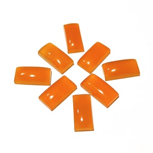 Puede incluir: Una colección de ocho gemas rectangulares de color naranja dispuestas en un patrón circular. Cada piedra tiene una superficie lisa y pulida y una forma ligeramente redondeada. Las gemas están sobre un fondo blanco.