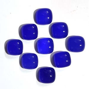 Puede incluir: Nueve gemas azules pulidas, de corte cuadrado con esquinas redondeadas, dispuestas sobre una superficie blanca. Cada piedra tiene un acabado brillante y refleja la luz. Las gemas son de un azul profundo y saturado.