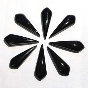 May include: Eight black, teardrop-shaped pendants arranged in a circular pattern. Each pendant has a smooth, glossy surface and a pointed tip. The pendants are displayed against a white background.