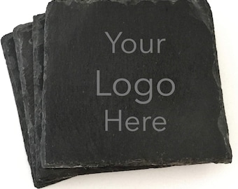 May include: A stack of four square, dark gray slate coasters. The coasters have a rough, natural edge and feature the text "Your Logo Here" in a light gray font. The coasters are stacked slightly offset from each other.