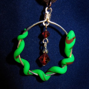 May include: A silver hoop necklace with a green and brown snake design and a dangling red crystal pendant.