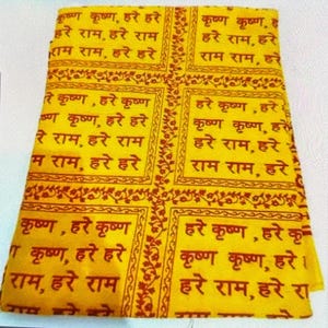 Può includere: Tessuto giallo con un motivo ripetuto di testo rosso scuro. Il testo sembra essere di natura religiosa, con ogni blocco di testo incorniciato da un bordo decorativo.