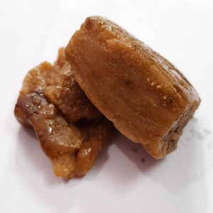 May include: Close-up of several pieces of a light brown, possibly fried, food item. The food has a slightly irregular shape and a glossy surface, suggesting it may be coated or glazed. The pieces are arranged on a white surface.