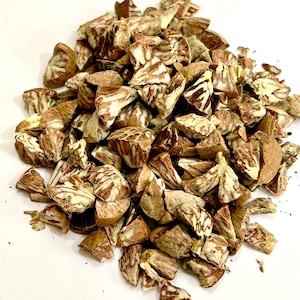 May include: A pile of chopped betel nuts, showcasing a mix of brown and cream colors. The nuts have a rough, textured appearance, with visible patterns and variations in color. The image is taken against a plain white background.
