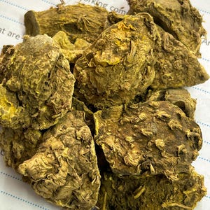 May include: A collection of dried turmeric rhizomes, showing a close-up view. The pieces are various sizes and shapes, with a textured surface and a mix of brown and yellow colours. The image is well-lit, showing the details of the dried turmeric.