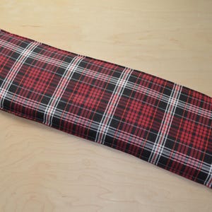 May include: A rectangular body pillow with a red, black, and white plaid pattern. The pillow is long and narrow, with a soft, fabric exterior. The plaid design features intersecting lines of red, black, and white.