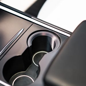 Peut inclure: Gros plan sur la console centrale d'une voiture, avec deux porte-gobelets et un design &eacute;pur&eacute;. Les porte-gobelets sont noirs avec des bordures argent&eacute;es, int&eacute;gr&eacute;s dans une console sombre et mate. L'int&eacute;rieur est minimaliste.
