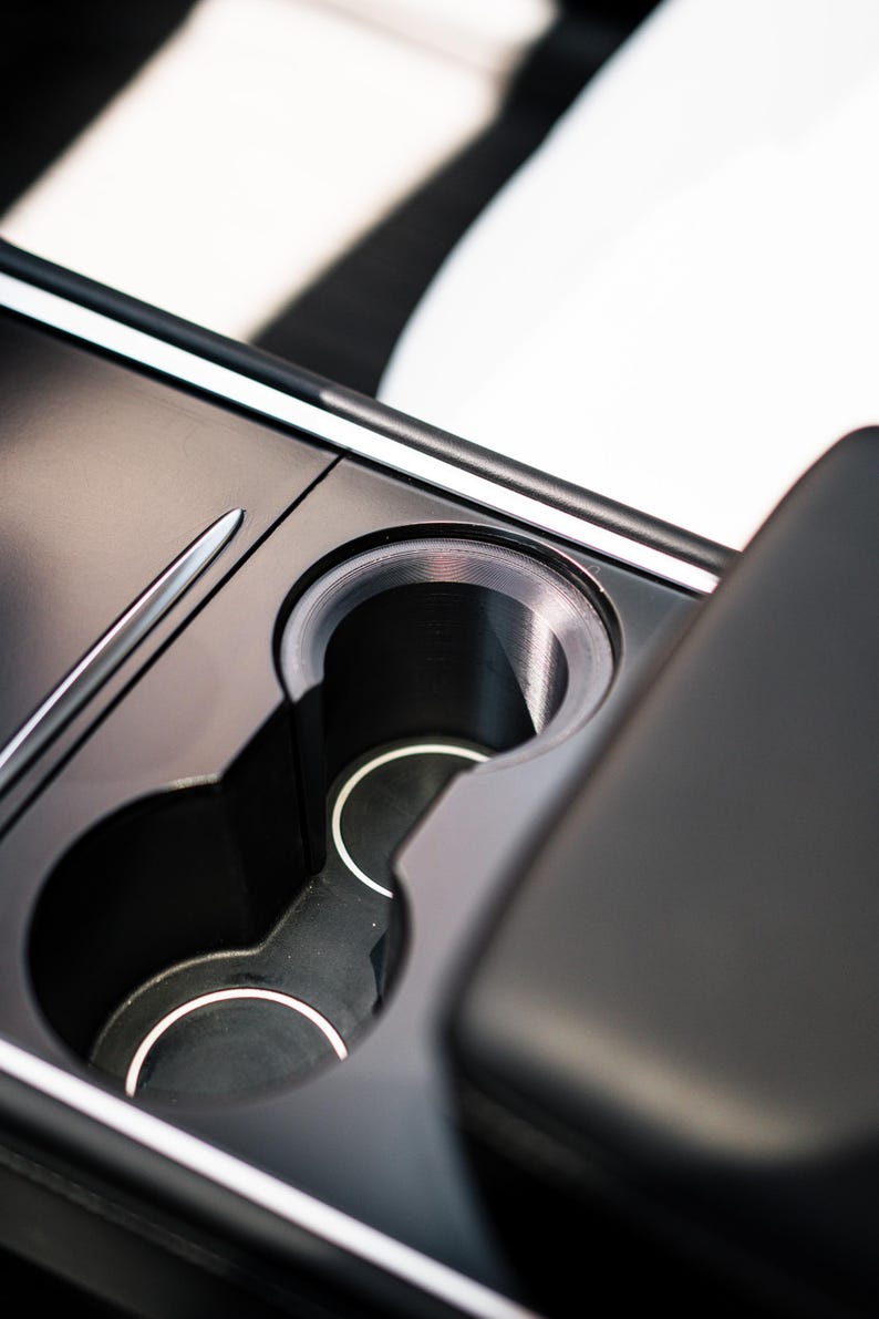 Peut inclure: Gros plan sur la console centrale d'une voiture, avec deux porte-gobelets et un design &eacute;pur&eacute;. Les porte-gobelets sont noirs avec des bordures argent&eacute;es, int&eacute;gr&eacute;s dans une console sombre et mate. L'int&eacute;rieur est minimaliste.