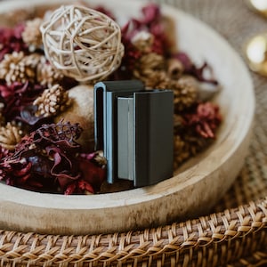 May include: A matte black rectangular belt clip holster featuring a sturdy vertical design with a smooth finish and a secure attachment mechanism, presented as a standalone functional accessory for carrying small rectangular items.
