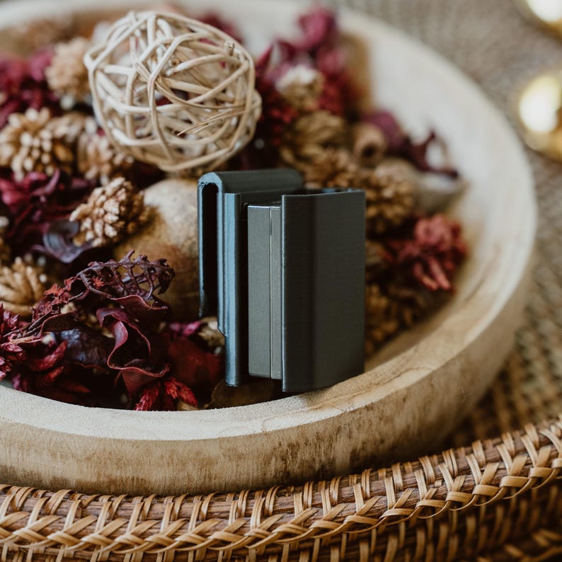 May include: A matte black rectangular belt clip holster featuring a sturdy vertical design with a smooth finish and a secure attachment mechanism, presented as a standalone functional accessory for carrying small rectangular items.
