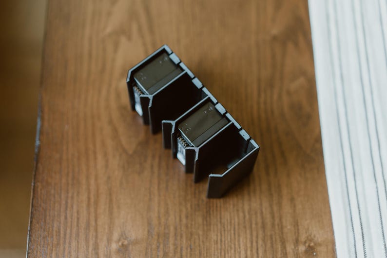 Peut inclure: Un organisateur noir rectangulaire &agrave; compartiments multiples, dot&eacute; d'une s&eacute;rie d'ailettes verticales et de fentes ouvertes. La structure est compos&eacute;e d'un mat&eacute;riau rigide au fini mat avec un motif g&eacute;om&eacute;trique r&eacute;p&eacute;titif pour les objets.