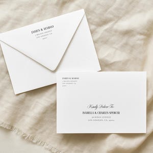 May include: Two white envelopes with black text on a beige linen surface. One envelope is closed, and the other is open, displaying the text "JAMES & MARGO" and an address. The open envelope reads "Kindly Deliver To ISABELLA & CHARLES SPENCER".