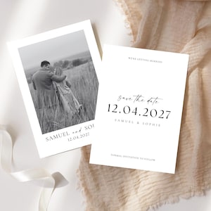 Peut inclure: Deux cartons d'annonce de mariage blancs. L'un présente une photo en noir et blanc d'un couple dans un champ. L'autre carte indique « Nous nous marions » et « Réservez la date 12.04.2027 » avec les noms Samuel et Sophie. Un ruban blanc et un tissu beige sont en arrière-plan.