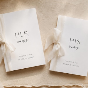 Può includere: Due libretti per i voti nuziali bianchi con nastri in chiffon color crema legati sul lato sinistro. Il libretto a sinistra riporta HER VOWS, quello a destra HIS VOWS. Entrambi presentano il testo NOVEMBER 19 2028 e OLIVER & SOPHIA in nero.