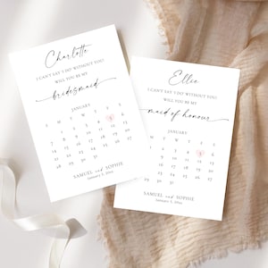 May include: Two white cards with calligraphy text, one reading "Charlotte, Will you be my bridesmaid?" and the other "Ellie, Will you be my maid of honour?". Each card has a calendar with a highlighted date. The cards are on a white surface.
