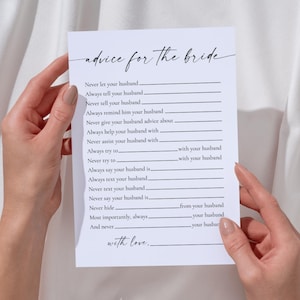 Op de afbeelding: Een witte kaart met de tekst "advice for the bride" in elegant schrift. De kaart bevat invulvragen voor advies, zoals "Never let your husband..." en "Always tell your husband...". De kaart wordt door twee handen vastgehouden.