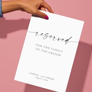 reserved wedding sign printable held by hand on blush pink background, minimalist wedding seating sign template, modern script wedding signage, editable Canva wedding sign download, clean aesthetic wedding decor