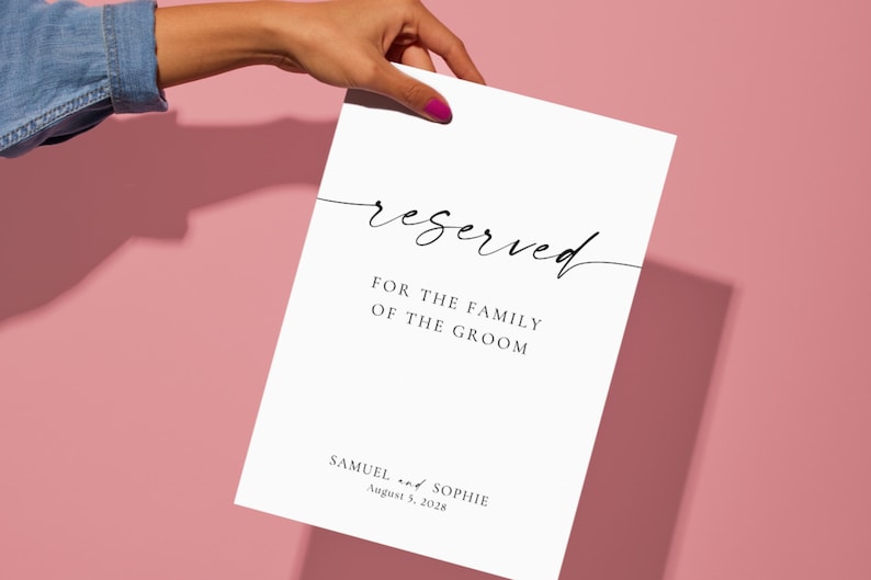 reserved wedding sign printable held by hand on blush pink background, minimalist wedding seating sign template, modern script wedding signage, editable Canva wedding sign download, clean aesthetic wedding decor