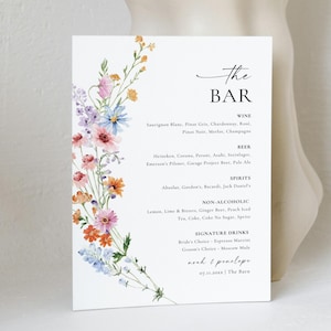 Puede incluir: Un menú de bar blanco con detalles florales en acuarela. El texto "The BAR" está en la parte superior, con categorías de bebidas y una lista de opciones. Un arreglo floral de flores rosas, azules y naranjas decora el lado izquierdo.