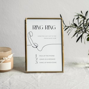 以下が含まれることがあります： 「RING RING」の文字と電話の線画が入った額縁入りのサイン。サインには「電話に出る、メッセージを残す、終了したら電話を切る」という指示も含まれています。瓶に入ったキャンドルと緑のある花瓶も画像にあります。