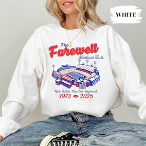 May include: White sweatshirt with a stadium graphic and the text "The Farewell Stadium Tour." The graphic includes the years 1973-2025 and the names Rich, Ralph, New Era, and Highmark. A casual, comfortable style.