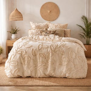 Könnte beinhalten: Cremefarbenes Bettwäsche-Set mit Blattmuster. Der Bettbezug und die Kissen haben erhabene Blattdesigns. Das Bett steht auf einem gewebten Teppich, mit dekorativen Kissen und einem gewebten Wandbehang. Eine Pendelleuchte aus Korbgeflecht hängt über dem Bett.