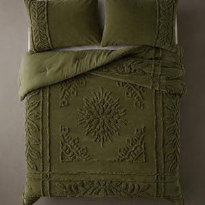 May include: An olive green bedding set consisting of a comforter and two matching pillow shams. The fabric features a raised, tufted texture with a central sunburst motif, geometric borders, and intricate leaf patterns across the surface.
