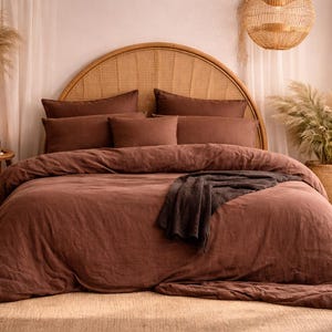 May include: A bed with a brown linen duvet cover and matching pillows. The headboard is made of woven rattan. Decorative elements include a woven pendant light, a basket, and a plant in a woven pot. The room has a neutral color palette.