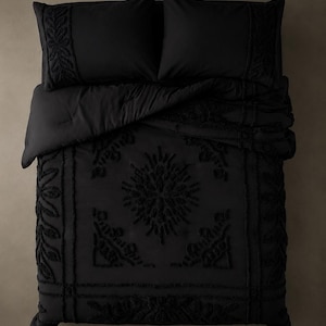 Può includere: Un set di biancheria da letto nero composto da un piumino e due federe abbinate. Il tessuto presenta un motivo floreale e geometrico in rilievo e testurizzato al centro e lungo i bordi, creando un design monocromatico sul letto.