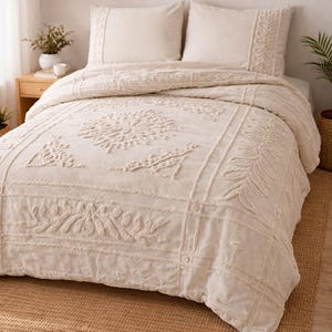 May include: Off-white bedding set featuring a tufted floral and leaf design. The set includes a duvet cover and two matching pillowcases. The bed is on a woven jute rug, and the room has a neutral colour scheme.