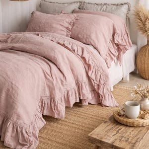 May include: A bed with pink ruffled bedding, including a duvet cover and pillowcases. The bed is on a woven jute rug, with a small wooden bench and a tray with a mug. A woven pendant light hangs above the bed.