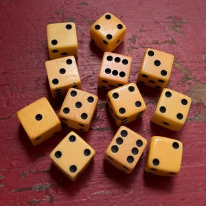 May include: A collection of eleven yellow six-sided dice with black pips scattered across the surface. Each die features standard numerical markings from one to six, with varying orientations showing different face values across the group.