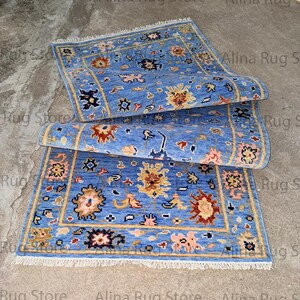 Könnte beinhalten: Zwei blaue Teppiche mit aufwendigen Blumenmustern und einem cremefarbenen Fransen. Die Teppiche sind aufgerollt und zeigen das detaillierte Design. Die Teppiche haben einen hellblauen Hintergrund mit gelben, roten und rosa floralen Akzenten.