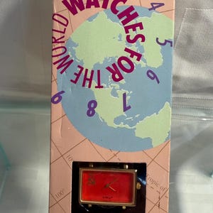 May include: A rectangular red watch with gold-colored accents is displayed in a box. The box has a world map graphic with the words "WATCHES FOR THE WORLD" and the brand name "FLAGTIME".