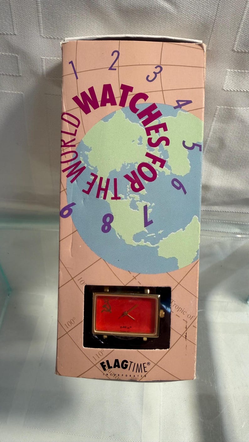 May include: A rectangular red watch with gold-colored accents is displayed in a box. The box has a world map graphic with the words "WATCHES FOR THE WORLD" and the brand name "FLAGTIME".