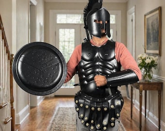 Könnte beinhalten: Schwarzes spartanisches Rüstungsset, einschließlich eines Helms mit hohem Kamm, Brust- und Armpanzerung sowie eines Schildes. Die Rüstung hat ein detailliertes, strukturiertes Aussehen. Der Schild ist rund mit einem stilisierten Design.
