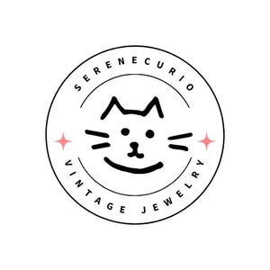 Może przedstawiać: Okrągłe logo z napisem "SERENECURIO VINTAGE JEWELRY" otaczającym twarz kota z kresk&oacute;wki. Twarz kota jest czarna z wąsami i uśmiechniętymi ustami. R&oacute;żowe rozbłyski gwiazd flankują twarz kota.