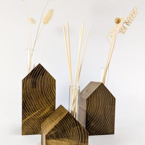 May include: A collection of wooden house-shaped ornaments in different sizes, stained a warm brown with visible wood grain. Clear glass test tubes contain dried flowers and reed diffusers, creating a natural, minimalist aesthetic. Set against a white background.