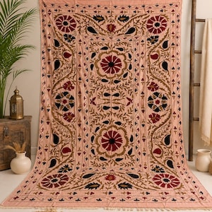 May include: A rectangular textile wall hanging in a light peach hue featuring intricate embroidery in deep red, black, and olive green. The design displays large floral motifs and paisley shapes arranged in a symmetrical pattern with fringe edges.