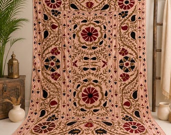 May include: A rectangular textile wall hanging in a light peach hue featuring intricate embroidery in deep red, black, and olive green. The design displays large floral motifs and paisley shapes arranged in a symmetrical pattern with fringe edges.