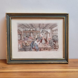 May include: Framed print depicting a gathering of men in a vintage setting. The artwork features a detailed interior scene with figures around a table, set within a black and gold frame. The frame rests on a wooden surface.