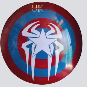 May include: A circular shield in red, white, and blue. It has concentric rings of red and blue, with a white star and a white spider design in the center. The letters "UK" are visible at the top of the shield.