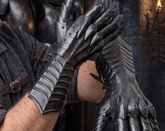 May include: A pair of articulated dark metal gauntlets featuring overlapping steel plates, pointed finger segments, and small rivets. These protective hand coverings are constructed with multiple hinged sections that allow for movement and flexibility.